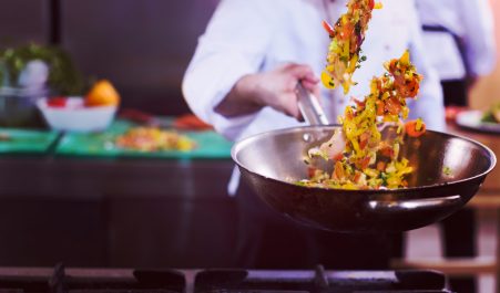 Young male chef flipping vegetables in wok at commercial kitchen